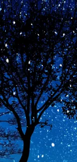 Silhouetted tree against starry blue night sky with falling snow.