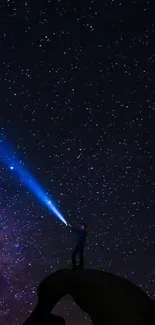 Silhouette holding flashlight under starry night sky.