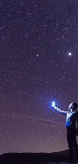 Person beneath a star-filled night sky with a glowing light.