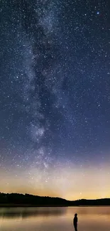 Silhouette by a lake under a starry night sky.