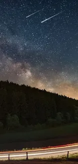 A starry night sky over a winding road surrounded by a dark forest.