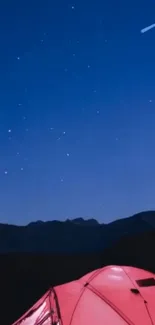 Starry night sky with red tent against mountain backdrop.