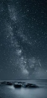 Starry night sky with Milky Way over ocean rocks at night.