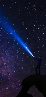 Silhouette on rock under starry night sky with flashlight beam.