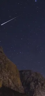 Starry night sky with shooting star over mountain peaks.