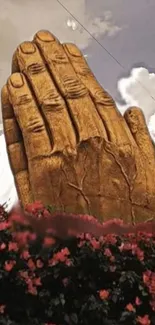 Stone hand sculpture with flowers and sky in the background.