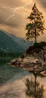 A lone tree on rocks by a mountain lake with lightning in the background.