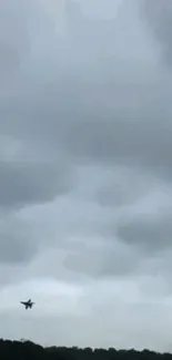 Silhouette of a jet flying beneath stormy gray clouds.