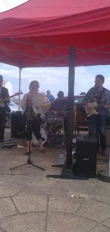 Street band performing under a red canopy.