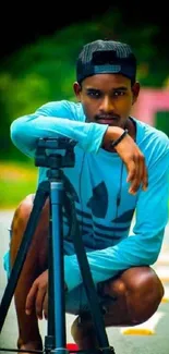 Young photographer with tripod on a street, wearing a blue shirt.