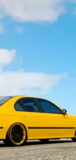 Vibrant yellow car under a clear blue sky with scattered clouds.