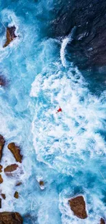 Aerial view of ocean waves crashing against rocky shore in vibrant blue hues.