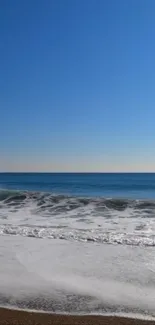 Calm ocean waves under a clear blue sky on a serene beach.