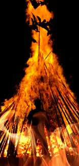 Silhouette of a person in front of a large bonfire at night.