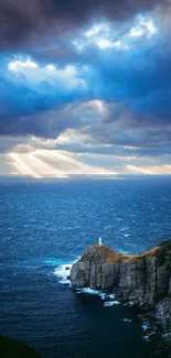 Lighthouse on rocky coast under dramatic sky with sun rays.