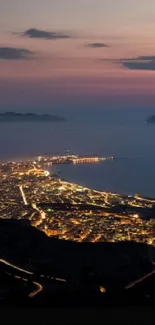 Coastal city lit up at dusk with islands on horizon.