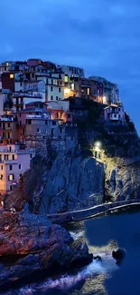 Illuminated cliffside village at night with blue seas.