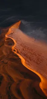 Aerial view of orange sand dune in desert landscape with dark sky backdrop.