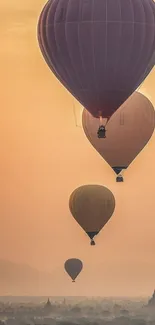 Four hot air balloons float over a misty landscape at sunrise with an orange sky.