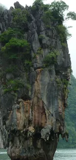 Towering island cliff surrounded by lush greenery and calm waters.