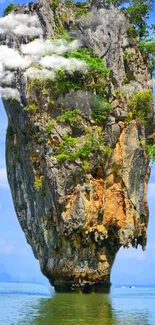 Towering island rock surrounded by blue water and green foliage.