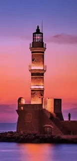 Lighthouse silhouetted at sunset by the ocean.