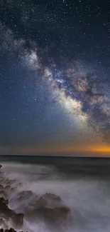 Milky Way galaxy shining over the ocean at night with rocks in the foreground