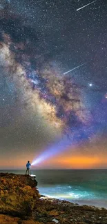 Person with flashlight under starry Milky Way on rocky coast.