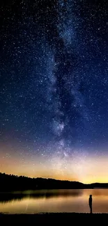 Milky Way galaxy above lake with silhouette of a person at night.