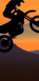 Motocross biker silhouette against a vibrant orange sunset over hills.