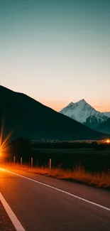 Scenic mountain road at sunset with glowing car headlights.