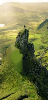 Man standing atop a green mountain peak with a scenic landscape view.