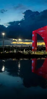 Night skyline with red arch and water reflection.