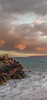 Serene sunset over a rocky ocean shore with dramatic clouds.