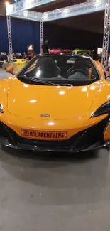 Orange sports car displayed at an indoor auto show.