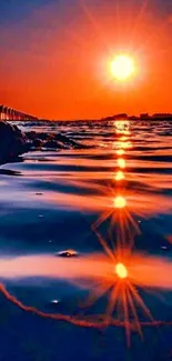 Orange sunset over ocean with vibrant reflection on water.