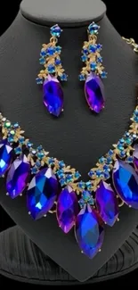 Purple and blue gemstone necklace with matching earrings displayed on black stand.