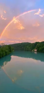 Rainbow arches over a lake with calm waters and lush greenery.