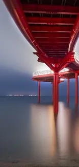 Red bridge extends over calm sea under a gradient sky.