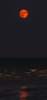 Red moon reflecting over a dark ocean horizon at night.