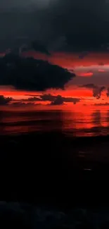 A breathtaking red sunset over a tranquil ocean horizon with dark clouds.