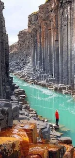 Person standing in a canyon with tall basalt columns and turquoise river.