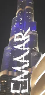 Skyscraper at night illuminated with blue lights and a striking city backdrop.