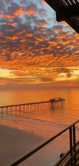 Beautiful sunset over a tranquil beach with an orange sky and pier silhouette.