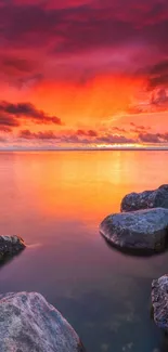 Stunning sunset beach with orange and purple sky over calm sea and rocks.