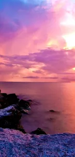 Purple and pink sunset over the ocean with rocky shore.