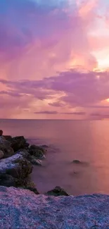 Colorful sunset over rocky coastline with pink sky and calm ocean.