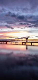 Silhouette on pier at sunset with stunning lavender sky reflection.