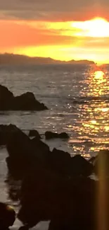 Sunset over rocky ocean shore with vibrant colors.