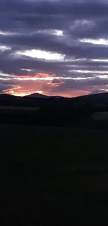 Twilight landscape with sunset over hills and dark sky.